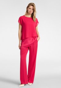 Completo a due pezzi in un vivace rosa, composto da una blusa fluida a maniche corte e pantaloni a gamba larga, entrambi in tessuto leggero.
