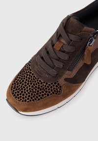 Basket marron avec tissu noir à motifs, empiècements en daim, lacets brun foncé et fermeture éclair latérale sur une semelle blanche.