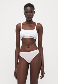 Brassière blanche avec une bande "HUGO" noire et un slip transparent assorti. Design simple, coupe ajustée, texture douce, style minimaliste.