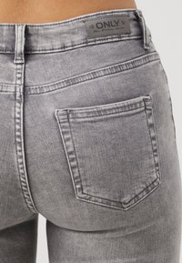 Gros plan sur la poche arrière et la ceinture d'un jean gris avec une étiquette indiquant "ONLY Blue Denim since 1995."