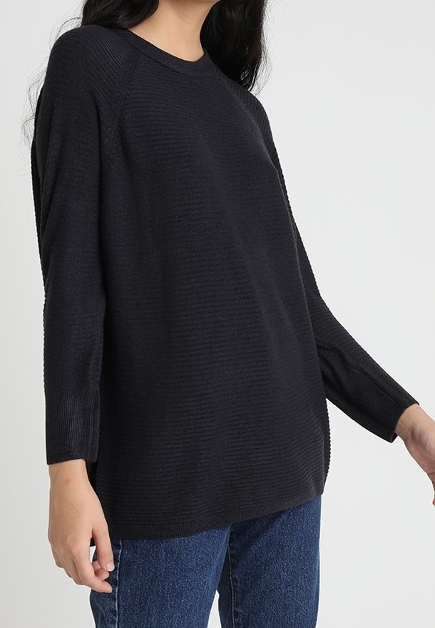 Schwarzer ribbeliger Pullover mit langen Ärmeln und Rundhalsausschnitt. Lockere Passform, kombiniert mit blauen Jeans. Glatte Textur.