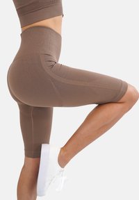 Shorts atletici marroni a vita alta realizzati in tessuto elastico, caratterizzati da una trama a coste e cuciture a contrasto, abbinati a sneaker bianche.