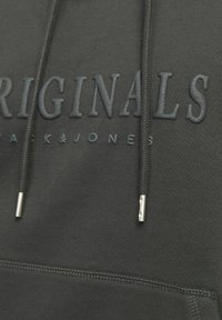 Ciemnozielona bluza z kapturem z wytłoczonym napisem "ORIGINALS", mocne sznurki z metalowymi końcówkami w kolorze srebrnym oraz teksturowana tkanina.