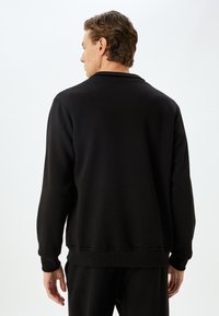 Svart sweatshirt med långa ärmar och ribbade manschetter och nederkant. Slät textur, klassisk passform, inga synliga logotyper eller mönster.