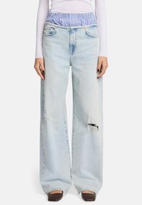 Helles blaues Weitbein-Jeans mit rissigen Knie-Details; dehnbarer Bund in blau-weißen Streifen; klassisches Fünf-Taschen-Design.