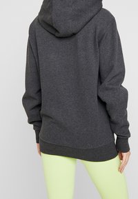 Sudadera gris carbón con capucha, que presenta una textura suave y puños acanalados. Combinada con leggings verde claro, que muestran un ajuste relajado.