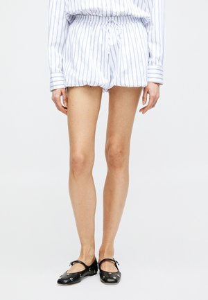 Personne portant un short à rayures blanches et bleues avec une taille à cordon, associé à des ballerines Mary Jane noires avec des détails en œillet argenté.