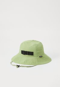 Chapeau seau en coton vert clair avec un large bord, texture matelassée et sangle noire réglable avec boucle sur le côté.