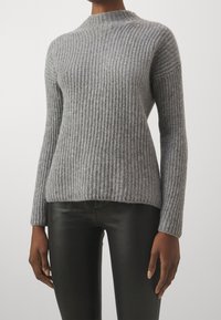 Maglione grigio lavorato a maglia con texture a coste, collo alto e maniche lunghe, abbinato a pantaloni neri aderenti.