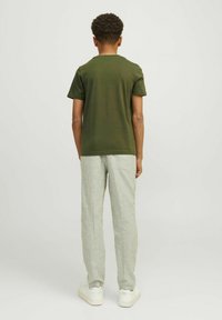 Grøn bomuld T-shirt, korte ærmer, kombineret med lysegrå linnedbukser og hvide sneakers, set fra ryggen.