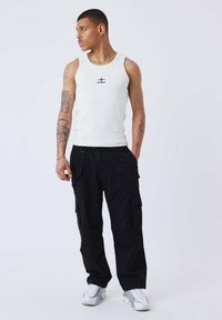 Top de tirantes blanco de algodón con un logo negro, combinado con pantalones cargo negros que tienen múltiples bolsillos y un corte holgado, completado con zapatillas ligeras.