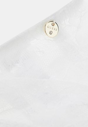 Witte kantenstof met een klein rond gouden label gegraveerd met "GUESS" en een kleine heldere strass steentje bevestigd met een witte draad.