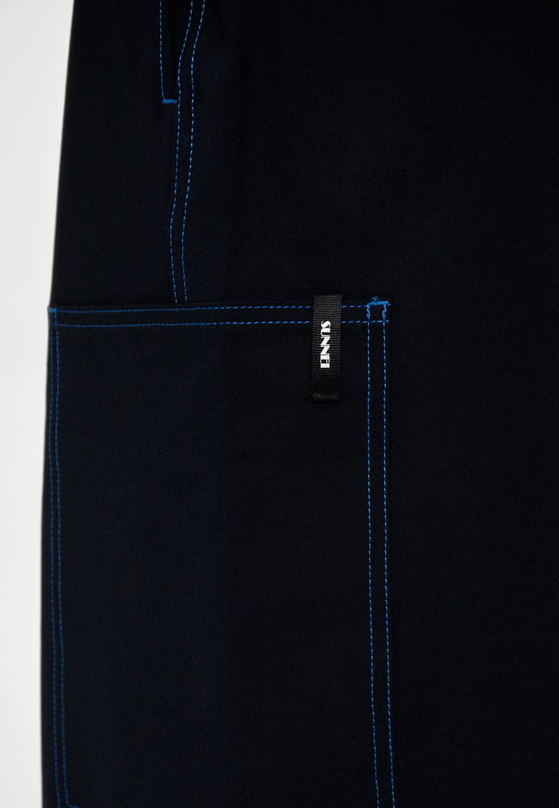 Dunkelblauem Stoff mit kontrastierendem blauen Nähten, strukturiertem Taschen mit einem Etikett und einem klaren, maßgeschneiderten Design.