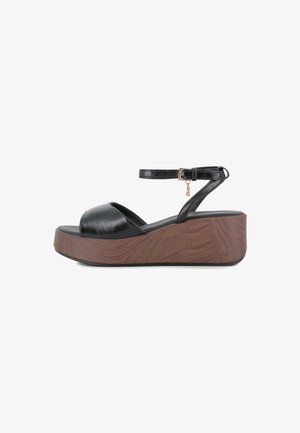 Sandalia cuña de cuero negro con punta abierta, suela plataforma de madera y una delgada correa en el tobillo con una pequeña hebilla dorada y un adorno.