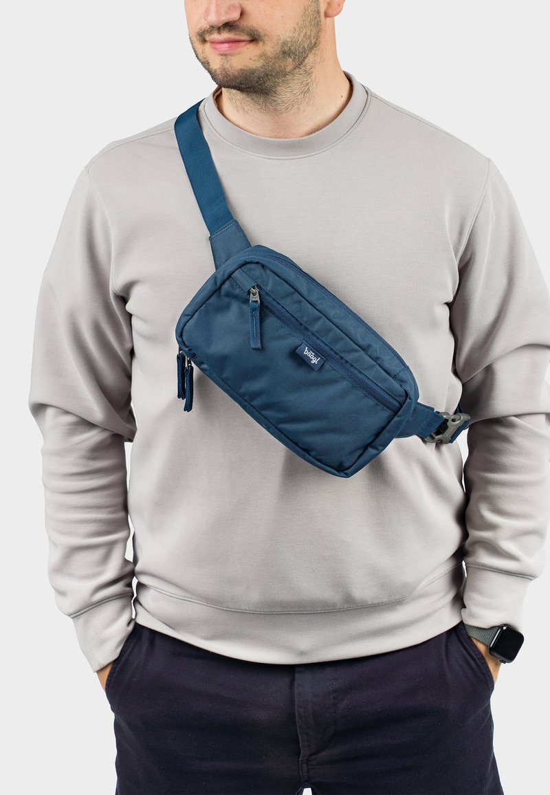 Borsa a tracolla in nylon blu navy indossata sul petto, con due scomparti con zip e una robusta tracolla regolabile, design razionalizzato.