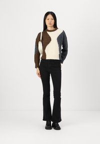 Strickpullover mit einem Farbabstufungsdesign in Braun, Creme und Blau; kombiniert mit schwarzen, ausgestellt geschnittenen Jeans und schwarzen Stiefeletten. Glatte Textur.