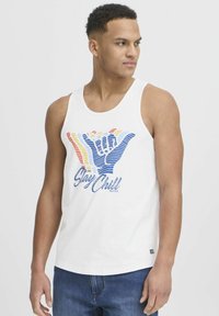 White cotton tank top featuring a graphic design of a hand sign in blue, red, and yellow, with the text "Stay Chill" below.