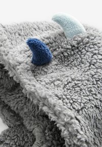 Grauem Plüschdecke mit weicher, flauschiger Textur; verfügt über zwei bunte Stoffhörner – eines blau und eines hellblau – die am Rand angenäht sind.