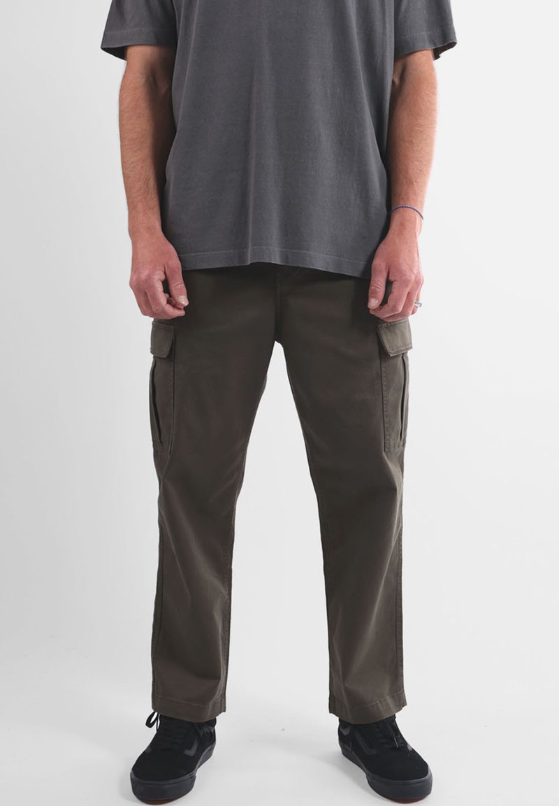 Pantalon cargo vert olive avec poches latérales, coupe droite, en tissu résistant. Associé à un t-shirt gris ample et des baskets noires.