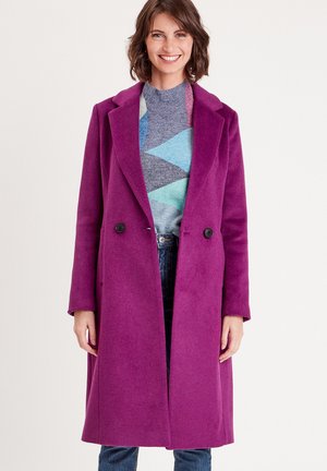 Purple wool blend coat with a double-breasted design, notch lapels, and two front pockets. Worn over a multicolored geometric sweater and jeans.