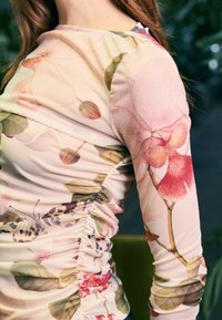 Langärmliges Oberteil aus elastischem Stoff mit floralen Mustern in sanften Rosa-, Grün- und Lilatönen und gerafften Details an der Seite.