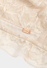 Lingerie in pizzo beige con motivi floreali, bordi in pizzo smerlato, una morbida fascia in satin e un piccolo tag metallico "Rosie" attaccato.