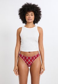 Weißes, ärmelloses Oberteil, kombiniert mit roten, karierten Bikini-Briefs mit einem Rüschensaum und kontrastierendem weißen Besatz. Glatter Stoff.