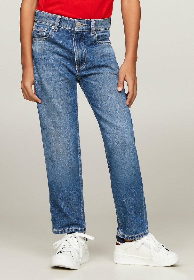 Jeans in denim blu con un design a gamba dritta, stile a cinque tasche e leggero sbiadimento. Indossati con sneaker bianche, con lacci e dettagli del logo.