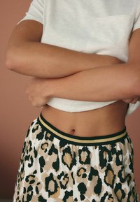 Leopardenmuster-Shorts mit einem elastischen Bund in Schwarz und Gold, kombiniert mit einem hellgrauen, figurbetonten Oberteil. Fokussieren Sie sich auf die Texturen und Muster.