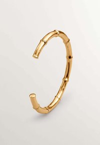 Pulsera de muñeca de metal en tono dorado, diseñada para parecerse a bambú, con formas segmentadas y curvas y un acabado pulido.