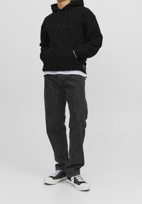 Zwarte hoodie met een buidelzak en logo-opdruk, gecombineerd met donkergrijze rechte jeans en zwarte sneakers met witte accenten.