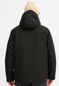 Zwarte geïsoleerde jas met een capuchon, met een gladde buitenkant en een licht gestructureerde stof. Inclusief zijzakken en een ontspannen pasvorm.