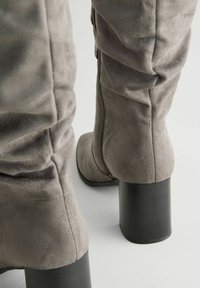 Graue Kunstsuede-Knielange Stiefel mit einem lockeren Design, ausgestattet mit einem seitlichen Reißverschluss und klobigen schwarzen hohen Absätzen. Weicher Stoff, minimale Nähte.