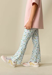 Pantaloni azzurri chiari con motivo floreale e tessitura a quadretti sottili, abbinati a sneaker bianche e pastello, e una camicia rosa.