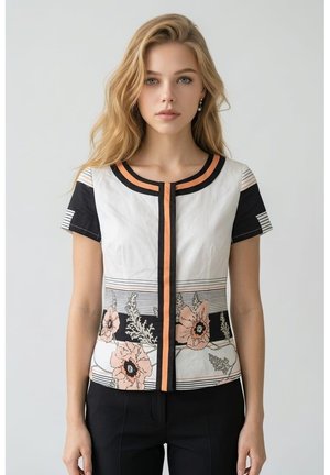 Joven mujer con cabello largo y rubio que lleva una blusa blanca con ribetes negros y naranjas y patrones florales, combinada con pantalones negros.