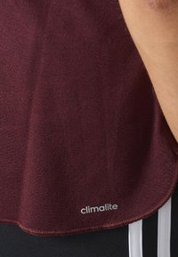 Burgundy idrottströja gjord av mjukt tyg, med rundad halsringning och en liten "climalite"-logotyp nära fållen, med en slät yta.