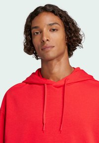 Röd hoodie med dragsko och avslappnad passform, tillverkad av mjukt tyg. Har en kenguruficka och en enkel design.