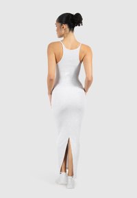 Eng anliegendes, knielanges weißes Kleid mit rundem Ausschnitt, dünnen Trägern und einem Rückenschlitz für Bewegungsfreiheit. Weiche, dehnbare Stoffstruktur.