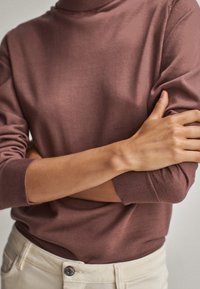 Mauve värinen korkeakauluksinen neulepaita pitkillä hihoilla, ribbireunuksilla ja sileällä pinnalla, yhdistettynä vaaleanvärisiin housuihin.