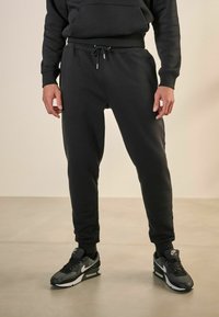 Svarta sweatpants med dragsko i midjan och ribbade ärmar, tillverkade av mjukt material. Matcher med svarta sneakers med vit accent.