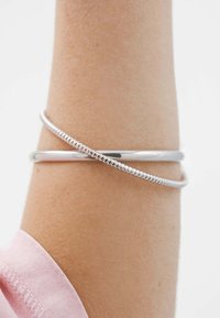 Dos pulseras de plata, una lisa y otra texturizada, llevadas en una muñeca con un puño visible de una manga rosa.