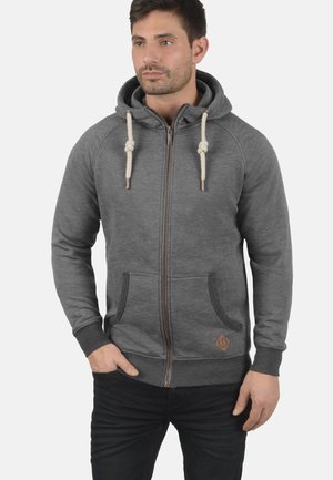 Grau zip-up Kapuzenpullover mit Zugband, vorderen Taschen und einem kontrastierenden braunen Logo-Patch. Weicher, strukturierter Stoff mit gerippten Bündchen und Saum.