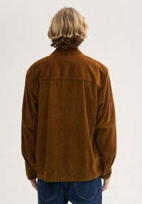 Brown corduroy jacket with a collar, long sleeves, and button cuffs. The fabric features vertical ridges and a relaxed fit.