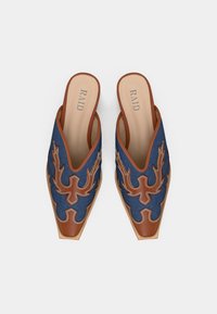 Denim mules med bruna läderdetaljer, spetsig tå och detaljerade sömmönster i kontrasterande färg. Varumärket "RAID" synligt på iläggsskorna.
