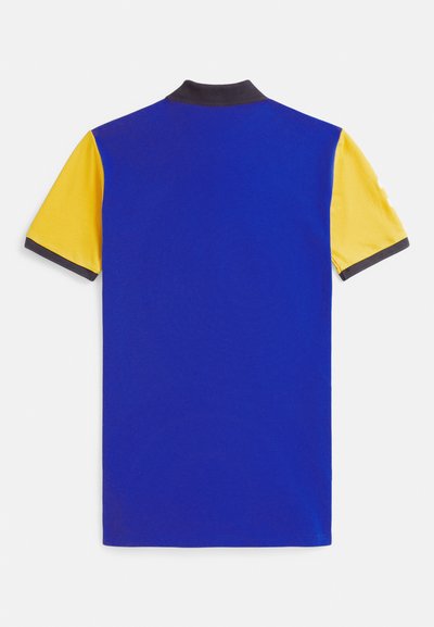 Trumpomis rankovėmis polo marškinėliai su karališkai mėlyna liemene, geltonomis rankovėmis ir juodu apykakle bei rankovių krašteliais, parodyti iš nugaros ant balto fono.