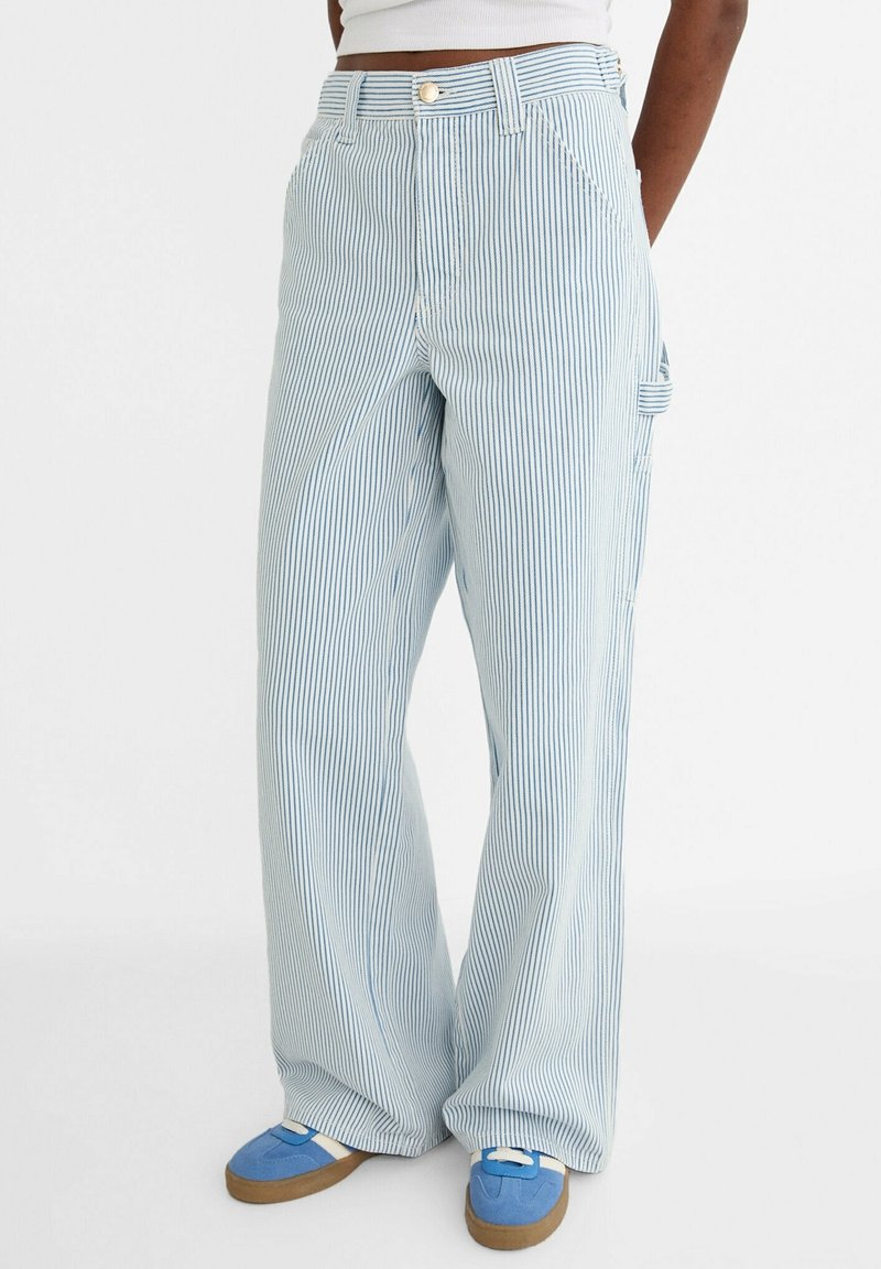 Pantalones de pierna ancha a rayas azul claro, hechos de tela transpirable, con bolsillos frontales y cierre de botón, combinados con calzado azul casual.