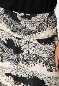 Jupe à motif floral noir et beige avec une taille smockée et des plis, fabriquée en tissu léger.