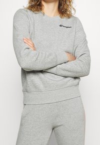 Sudadera de forro polar gris con cuello redondo, puños y cintura de canalé. Presenta un pequeño logotipo negro bordado en el pecho.