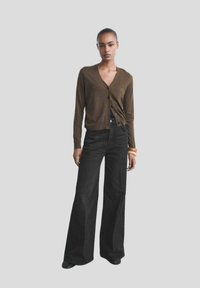 Cárdigan marrón con escote en V y seis botones negros, combinado con unos vaqueros negros de pierna ancha de alta cintura y una pulsera gruesa.