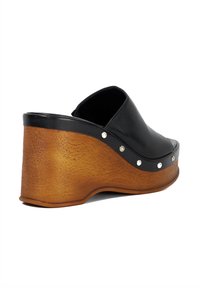 Black leather platform clog with a curved wooden sole and metallic studs along the side. Smooth texture, rounded shape, slight heel.
